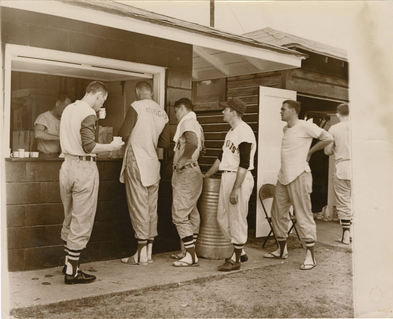 Black-and-white photograph of six Chattanooga Lookouts players standing at a concession stand, being served by a man who appears to be Sandy Sandlin.
