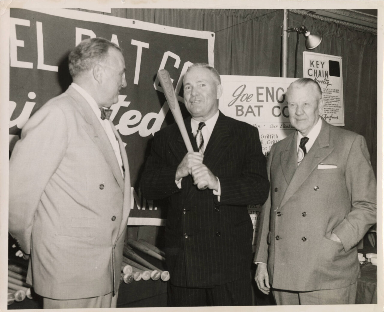 Black-and-white photograph of Joe Engel and two others standing in front of a display promoting the Joe Engel Bat Company. Pictured, left to right: Joe Engel; Rogers Hornsby, a Major League baseball player, manager, and coach who played for the Chattanooga Lookouts in 1938; and Zinn Beck, a minor league manager and scout.
