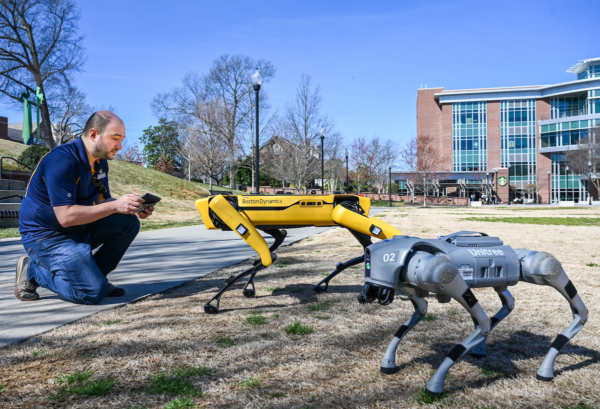 Gokhan Erdemir, Ann McAbee and Trevor Kight work Friday, Feb. 28, 2025 on Chamberlain Field to gather data from two robotic dogs, Spot and Goddard. The data will be compared against data from real dogs and used to make the robots move more like real dogs.