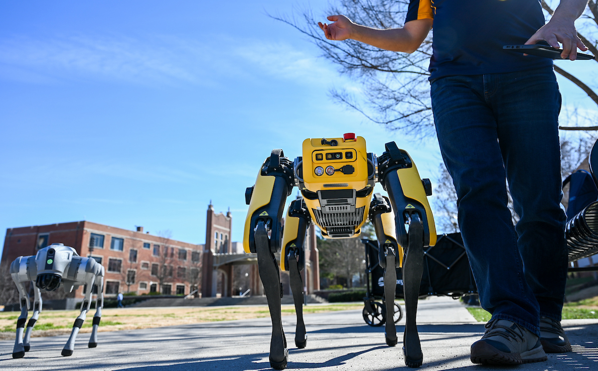 Gokhan Erdemir, Ann McAbee and Trevor Kight work Friday, Feb. 28, 2025 on Chamberlain Field to gather data from two robotic dogs, Spot and Goddard. The data will be compared against data from real dogs and used to make the robots move more like real dogs.