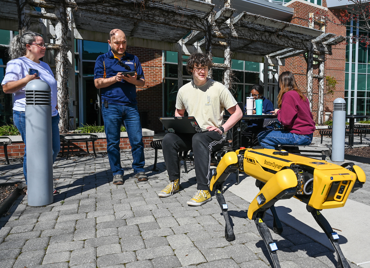 Gokhan Erdemir, Ann McAbee and Trevor Kight work Friday, Feb. 28, 2025 on Chamberlain Field to gather data from two robotic dogs, Spot and Goddard. The data will be compared against data from real dogs and used to make the robots move more like real dogs.