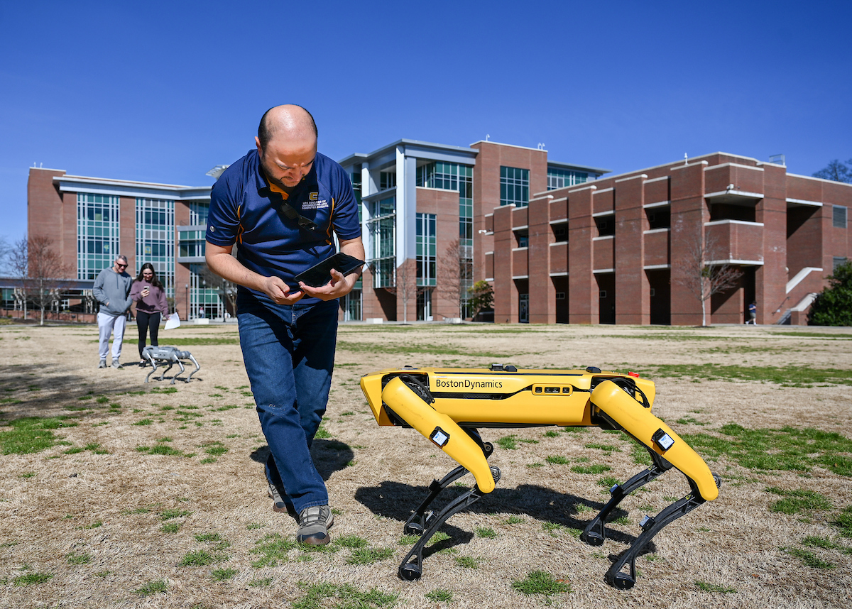 Gokhan Erdemir, Ann McAbee and Trevor Kight work Friday, Feb. 28, 2025 on Chamberlain Field to gather data from two robotic dogs, Spot and Goddard. The data will be compared against data from real dogs and used to make the robots move more like real dogs.