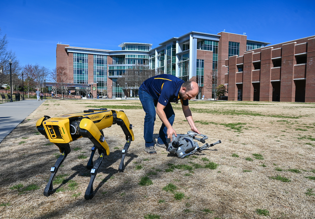 Gokhan Erdemir, Ann McAbee and Trevor Kight work Friday, Feb. 28, 2025 on Chamberlain Field to gather data from two robotic dogs, Spot and Goddard. The data will be compared against data from real dogs and used to make the robots move more like real dogs.