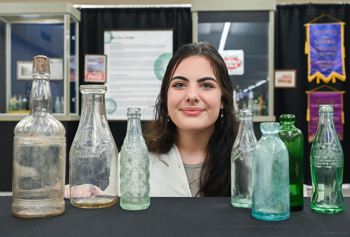 UTC history major Emily Kleiner, who helped curate "Glass from the Past," stands with a vintage glass display at the Chattanooga Public Library. Photo by Angela Foster.