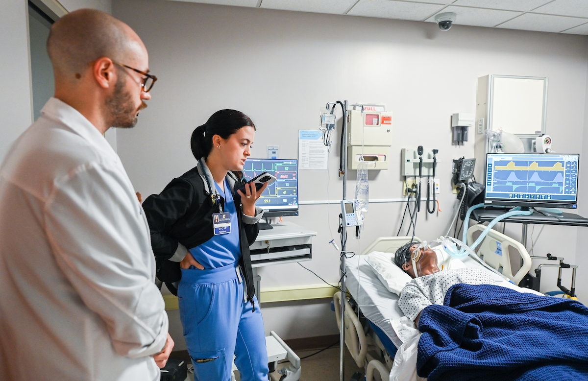 DNP acute care student Alexis Murray, under the watchful eye of Dr. Chris Doneski, talks with a patient's daughter during the AI simulation. Photo by Angela Foster.