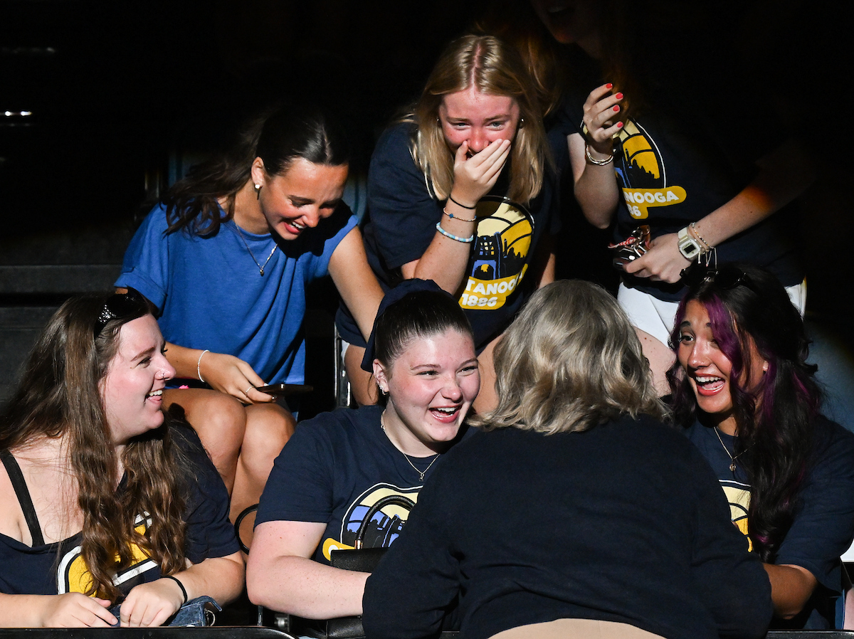 A group of students laugh as Chancellor Bruce (turned away from the camera) talks with them in the McKenzie Arena crowd at Convocation