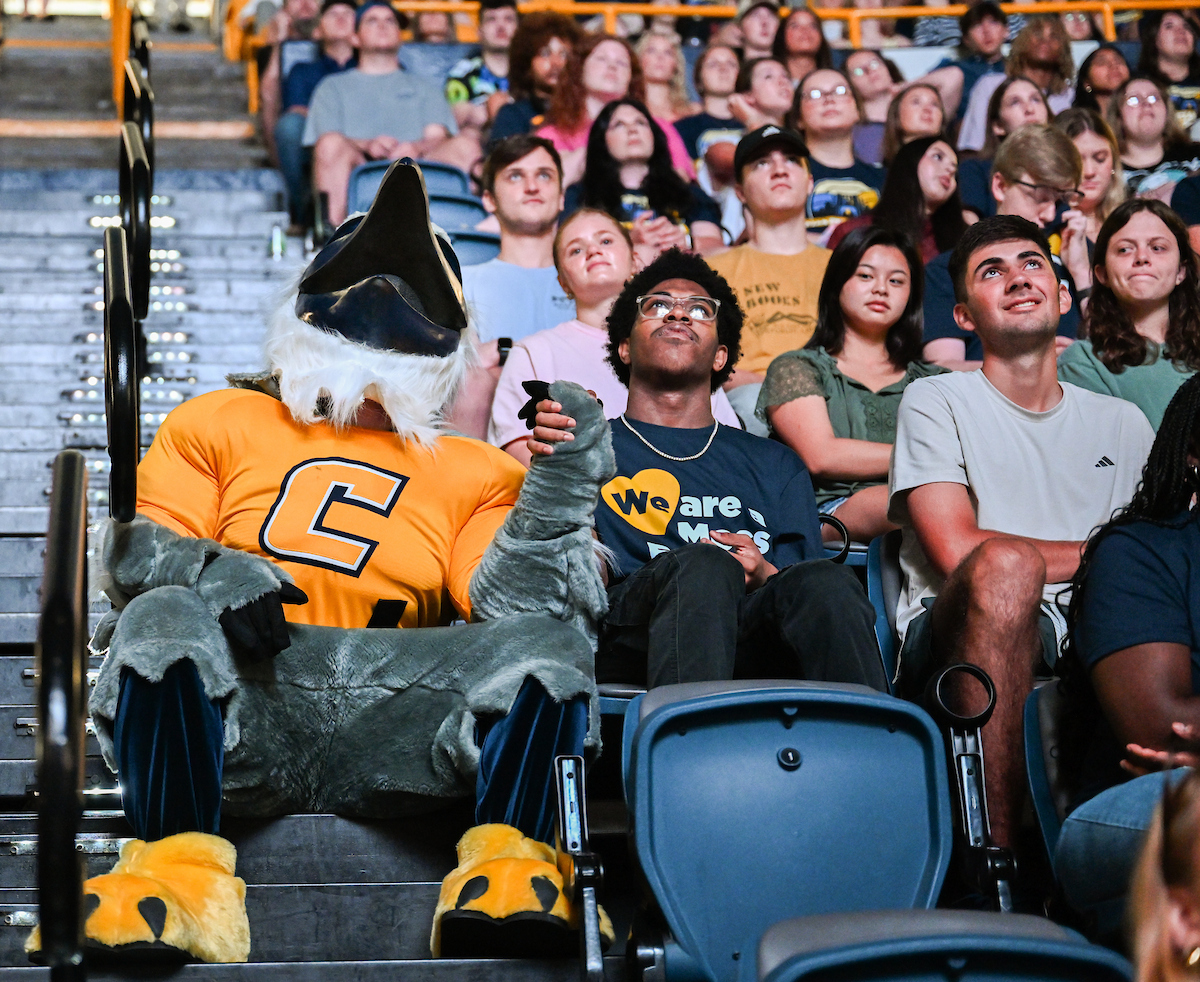 Scrappy holds hands and looks into the crowd with a student at Convocation in McKenzie Arena