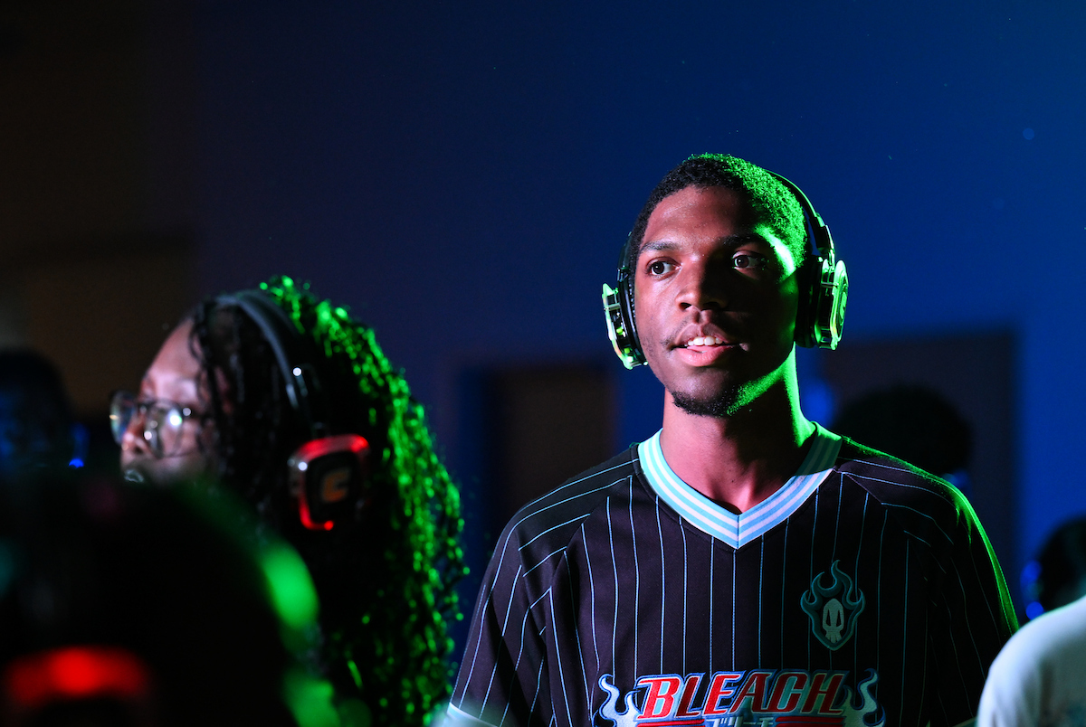 A student wearing headphones stands in colorful lighting, looking ahead during the silent disco event.