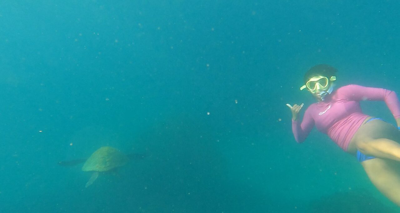 Roseline Gragg in a snorkeling mask swimming next to a green sea turtle underwater.