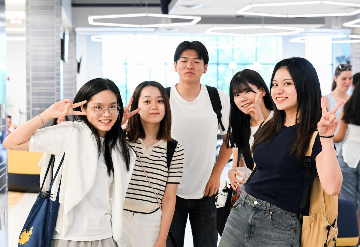 A group of five students pose together inside the University Center, smiling and making peace signs.