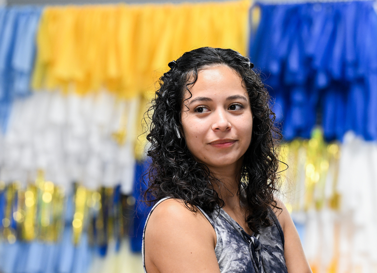 A student stands in front of blue and gold decorations, looking slightly off to the side.