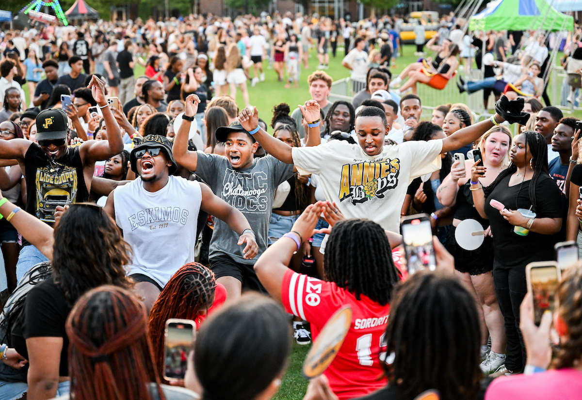 A group of students raise their arms and chant in front of a crowd at Welcome Week.