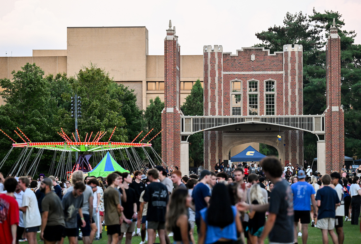 Students gather on Chamberlain Field during Welcome Week with the arches and carnival rides in view.