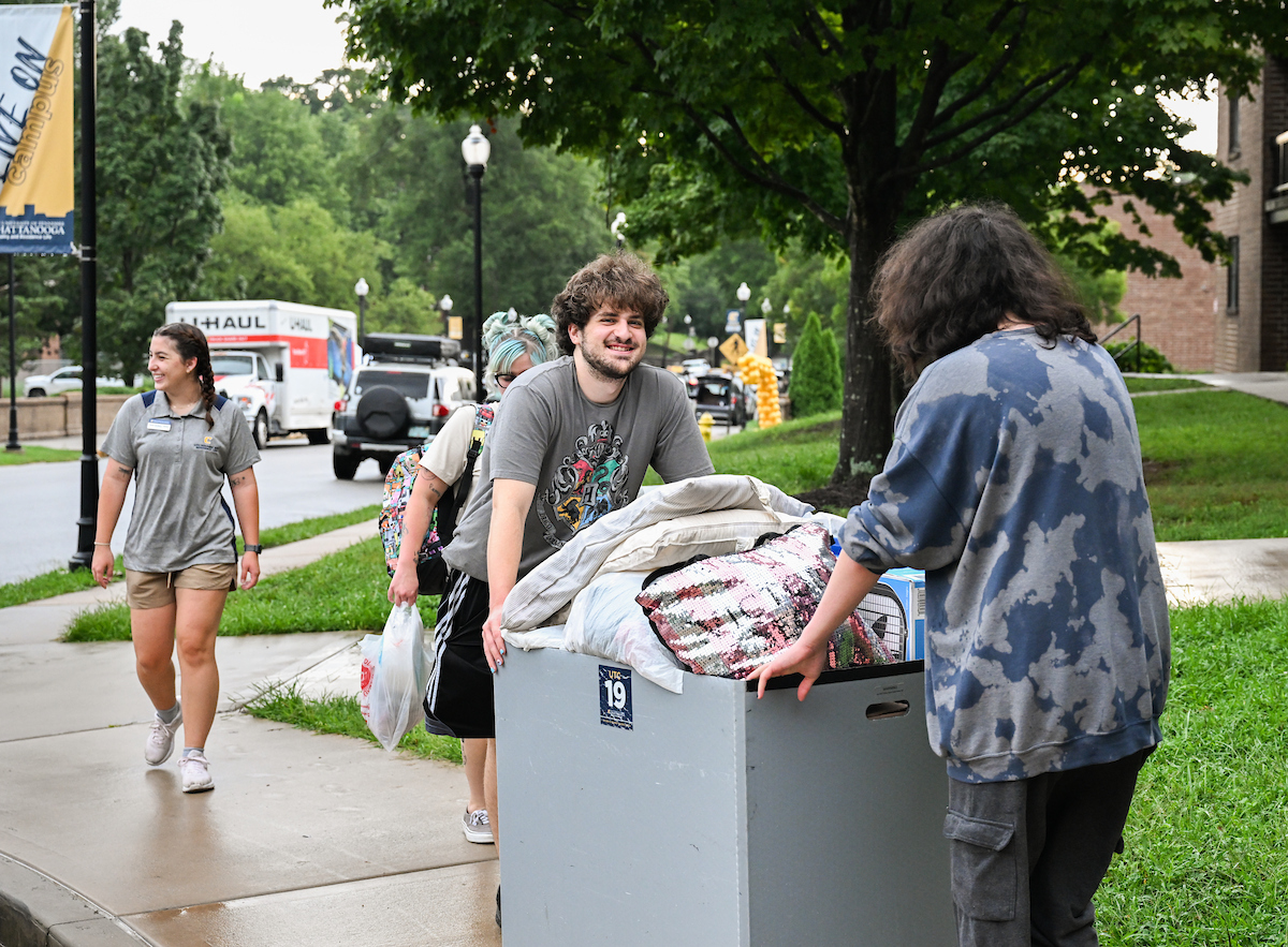 Volunteers help roll in a students belongings into West Campus Housing.