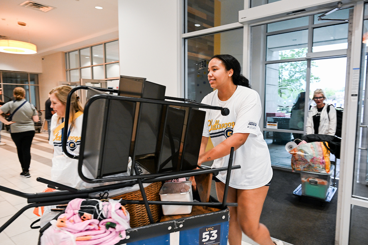 A volunteer pushes a cart of items into West Campus Housing.