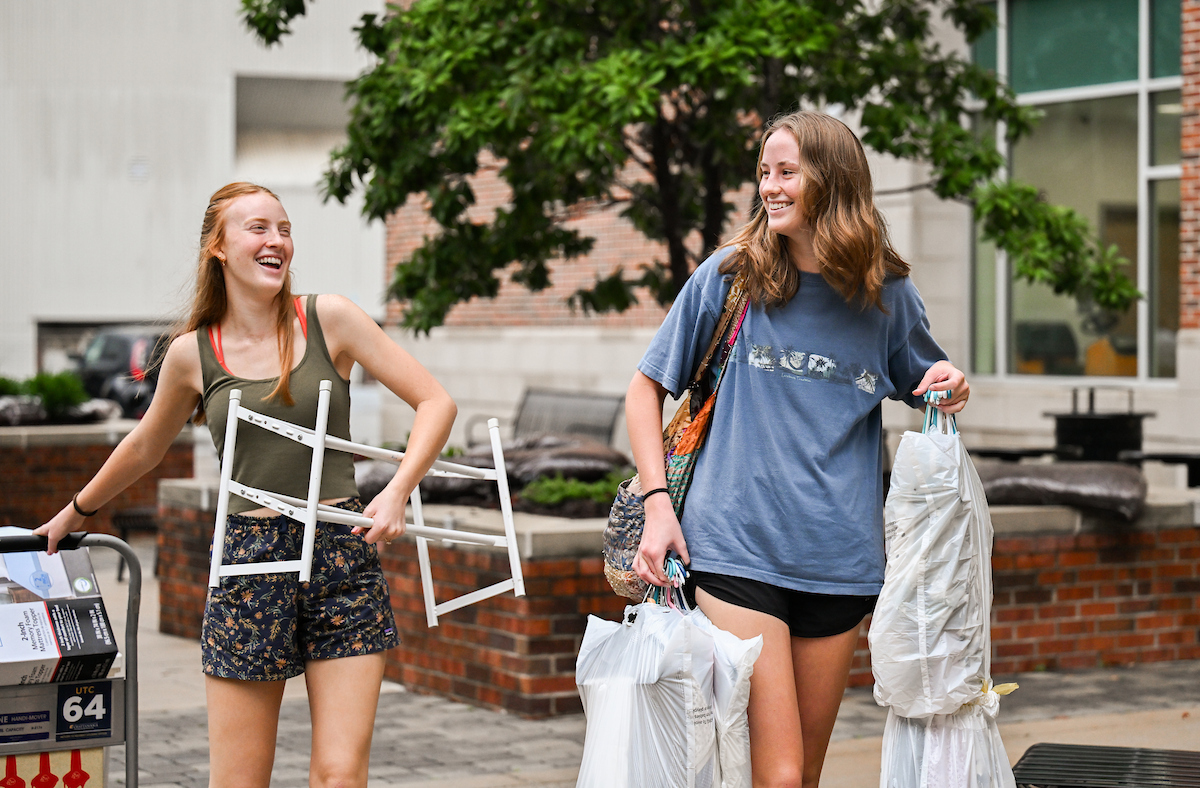 Two people carry belongings into West Campus Housing.