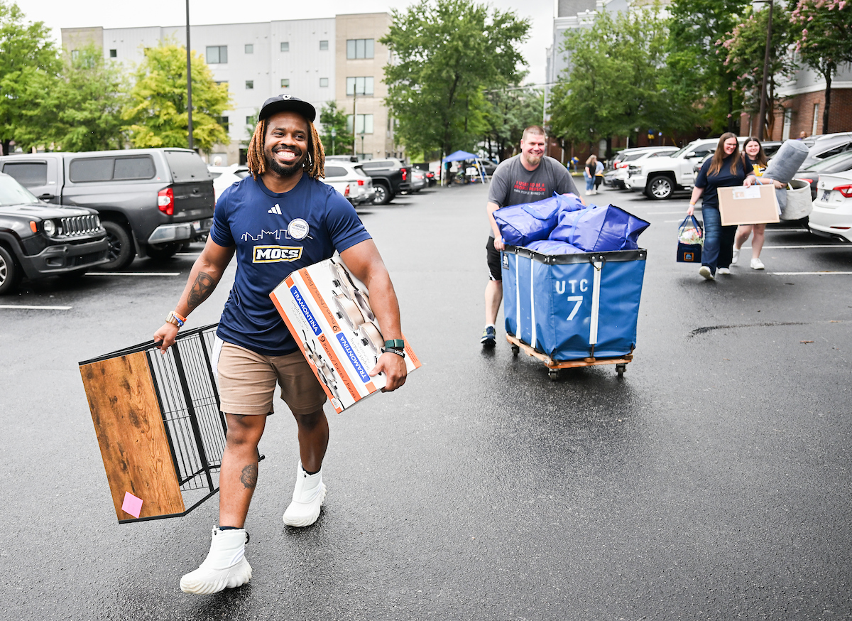Volunteers help carry and role a student's belongings into West Campus Housing.