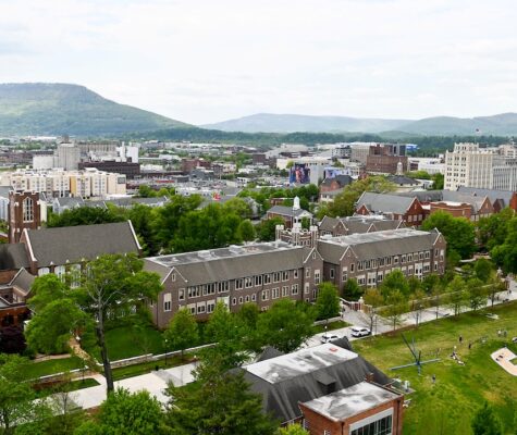 An aerial view of UTC and Chattanooga. Hooper and Race Halls are in the foreground along with the edge of Chamberlain Field, including the Power C. Downtown and mountains are in the background.