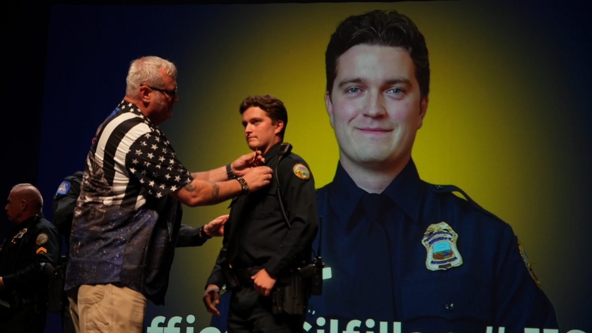 Chattanooga Police Department academy graduate John Glfillan gets pinned by his father with an image of Officer Gillifan on-screen behind them