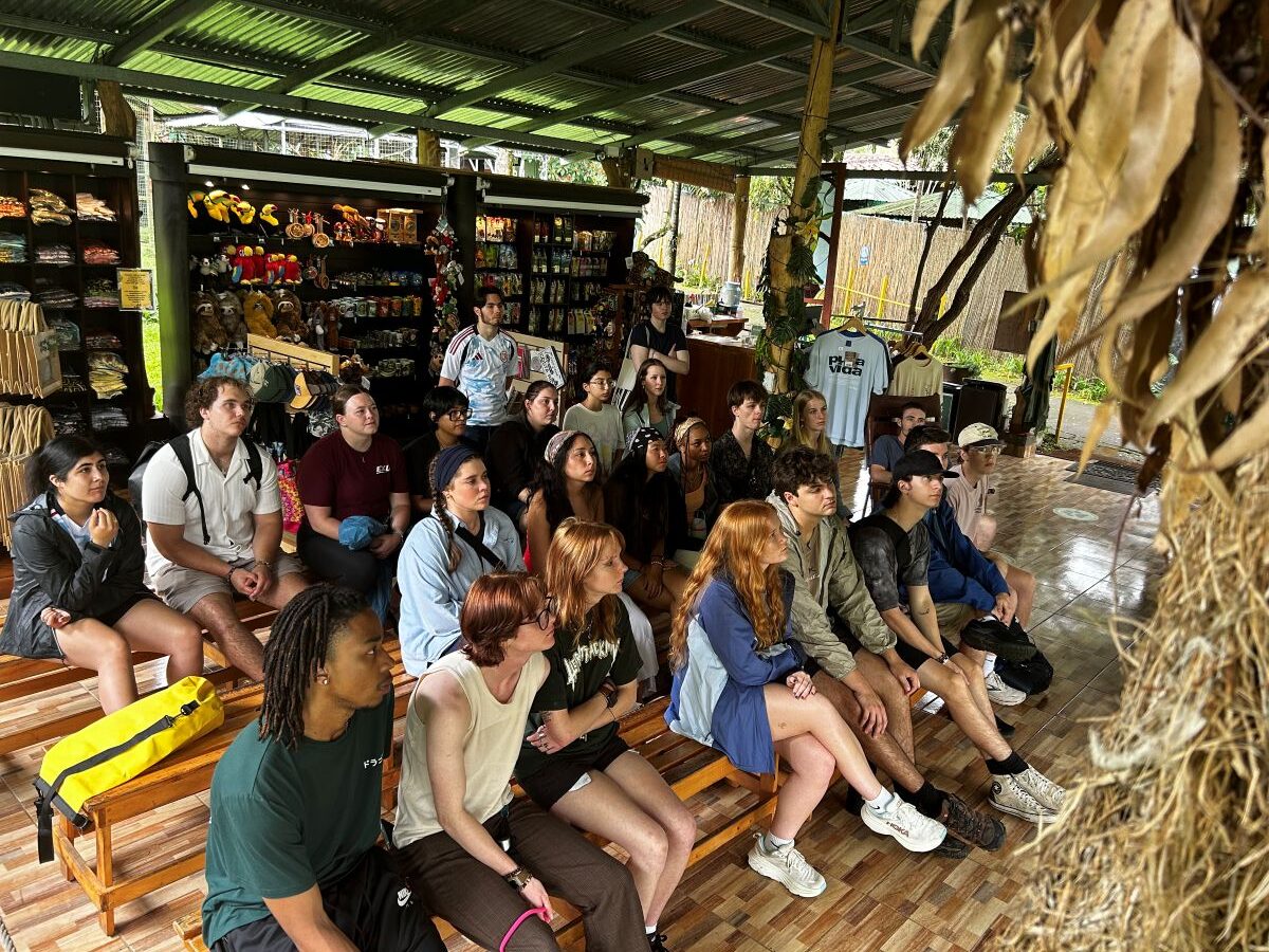 Group of UTC students sitting on wooden bleacher listening to a speaker
