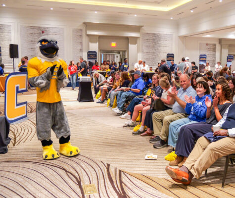 Scrappy stands in the front of the ballroom in front of hundreds of guests at a Power C Tour stop