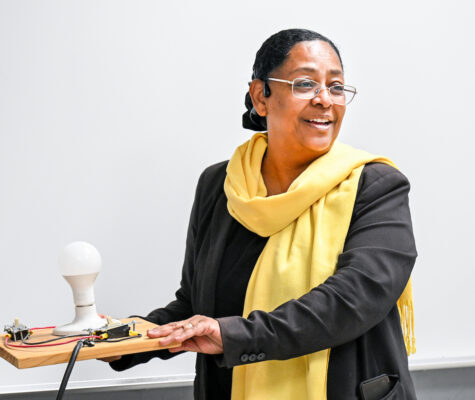 Dr. Raga Ahmed holding a piece of wood with a lightbulb on it during an introduction to electrical engineering class