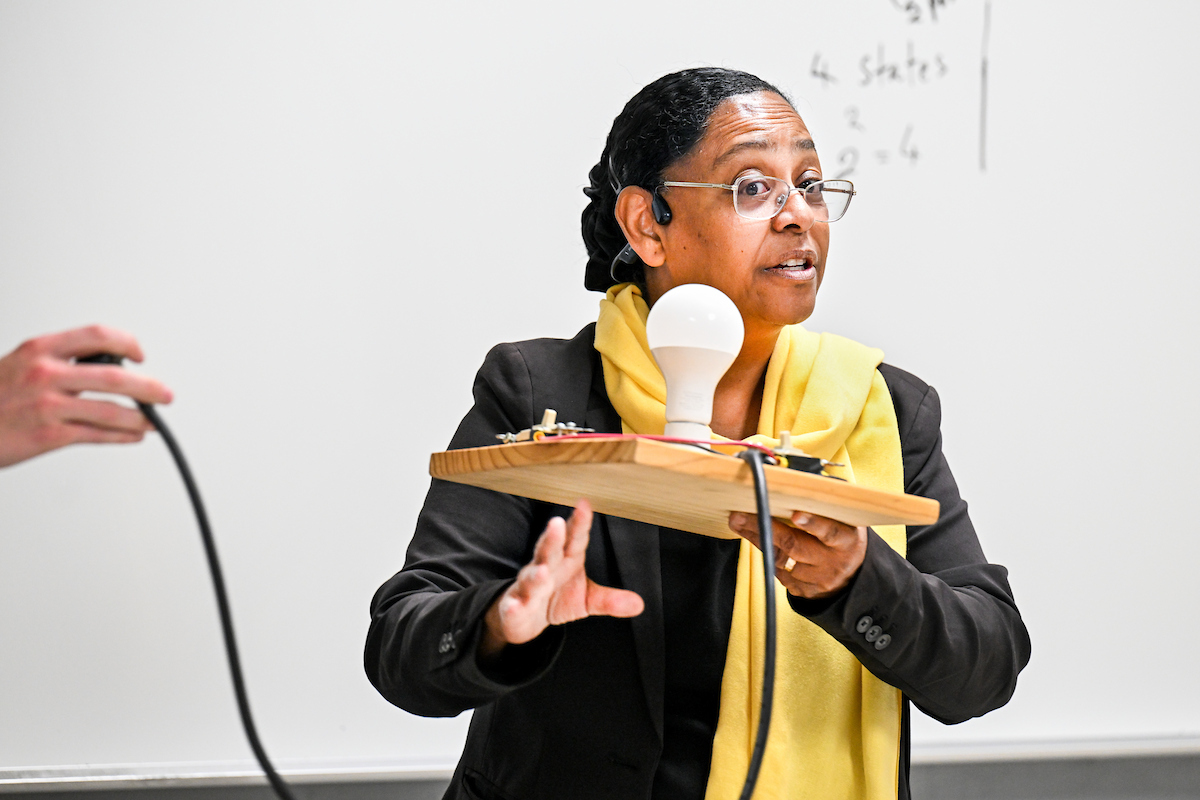 Raga Ahmed holds up a piece of wood with a light bulb on it as part of an Introduction to Electrical Engineering demonstration