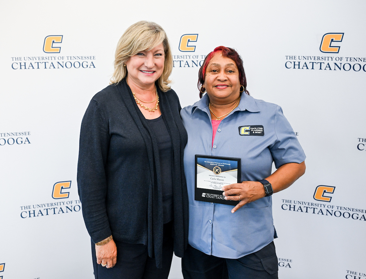 Chancellor Lori Bruce standing next to Carla Mason, who is holding a service award plaque, in front of a UTC-branded backdrop at the 2025 UTC Service Awards.