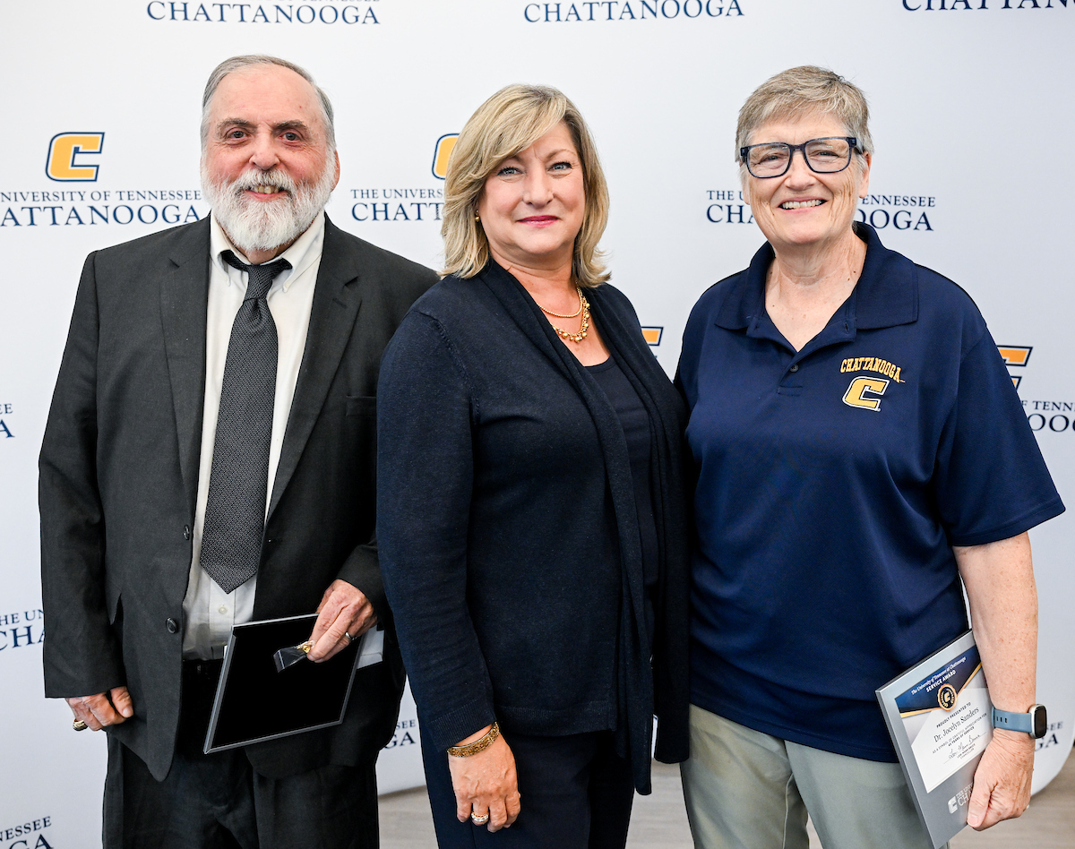 Dr. Gary McDonald, Chancellor Lori Bruce and Dr. Jocelyn Sanders standing together and smiling in front of a UTC-branded step-and-repeat backdrop at the 2025 UTC Service Awards.