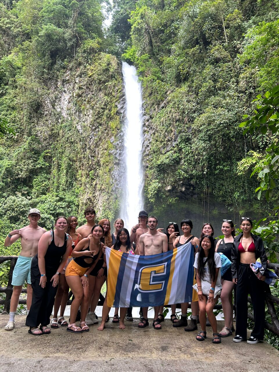 Group of UTC students standing with Power C flag in front of a waterfall