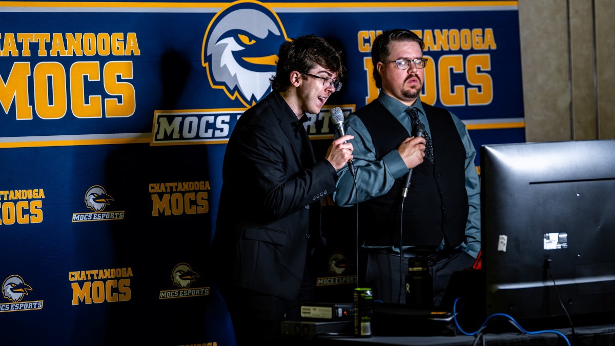 Two Twitch broadcasters calling a Rocket League game in front of a Chattanooga Mocs esports step and repeat