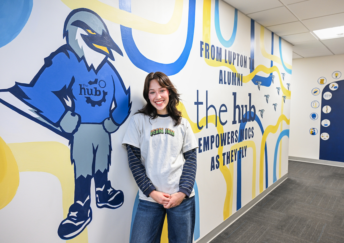 Sydney Zwart stands next to Scrappy in front of a mural that she painted