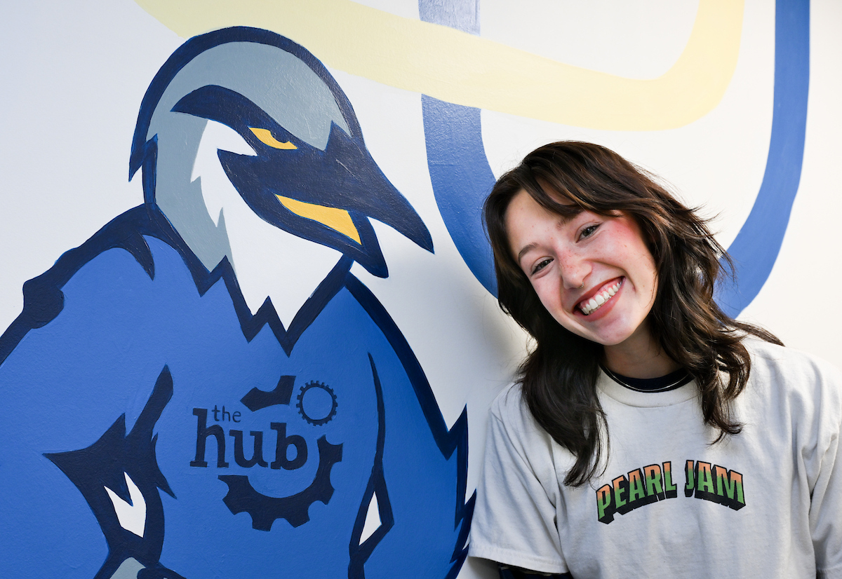 Sydney Zwart stands next to Scrappy as part of a mural that she painted
