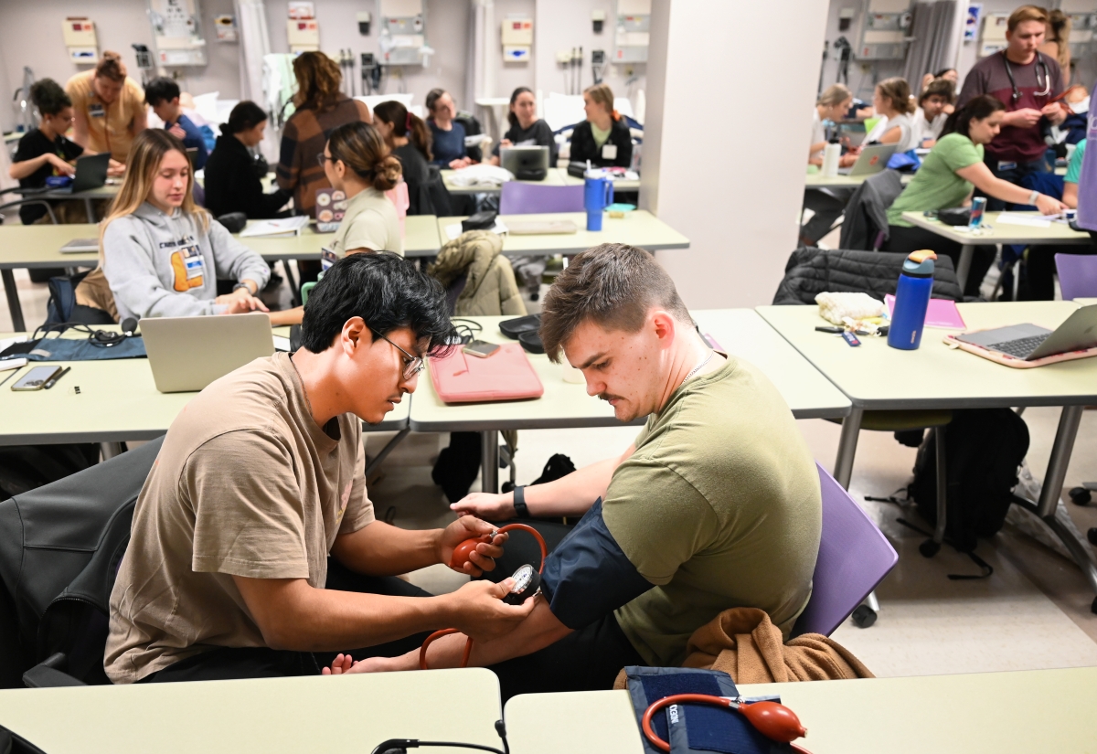 Nursing students practice taking vitals on each other, including blood pressure checks